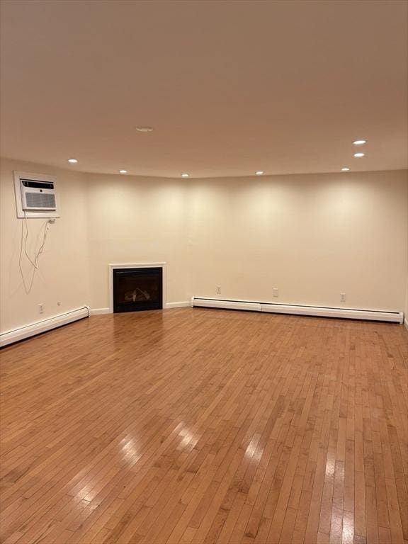 basement featuring hardwood / wood-style flooring, a baseboard heating unit, recessed lighting, an AC wall unit, and baseboard heating