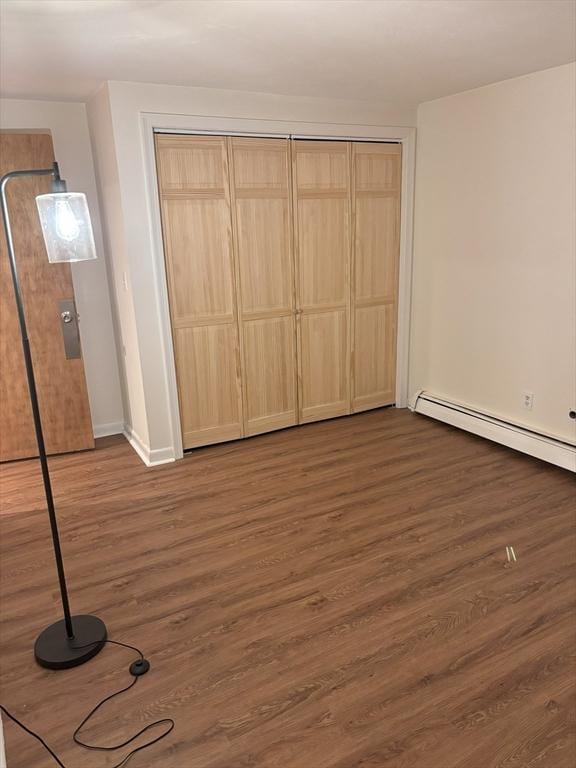 unfurnished bedroom with baseboards, dark wood-style flooring, a closet, and baseboard heating