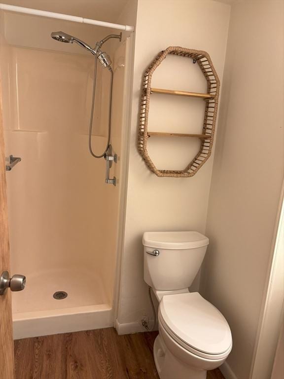 bathroom featuring toilet, baseboards, a shower stall, and wood finished floors