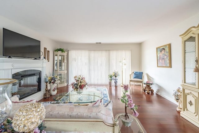 living room featuring a glass covered fireplace, visible vents, wood finished floors, and baseboards