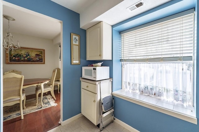 kitchen featuring white microwave, visible vents, baseboards, light tile patterned floors, and white cabinetry