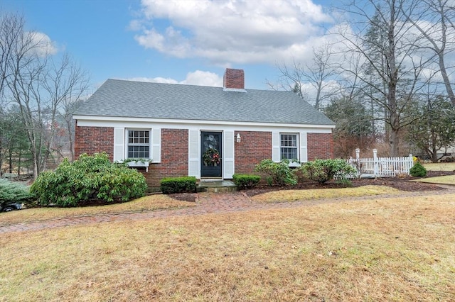 view of front of house featuring brick siding, a chimney, a front yard, and fence