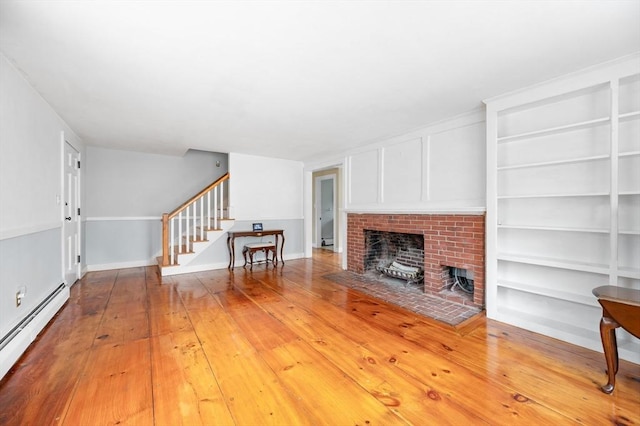 unfurnished living room featuring light wood finished floors, built in shelves, a baseboard radiator, stairway, and a fireplace