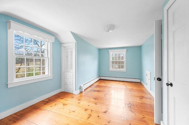 unfurnished bedroom featuring baseboards, vaulted ceiling, baseboard heating, a closet, and wood-type flooring