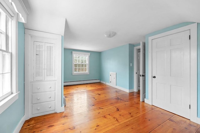 unfurnished bedroom featuring baseboard heating, light wood-type flooring, and baseboards