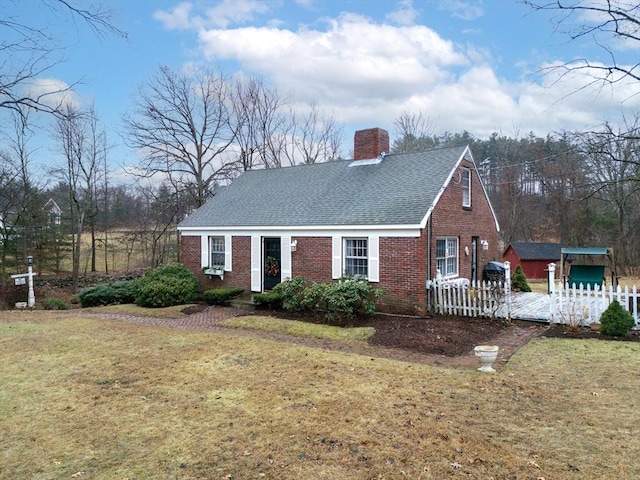 view of front of home featuring a shingled roof, a front yard, brick siding, and a chimney