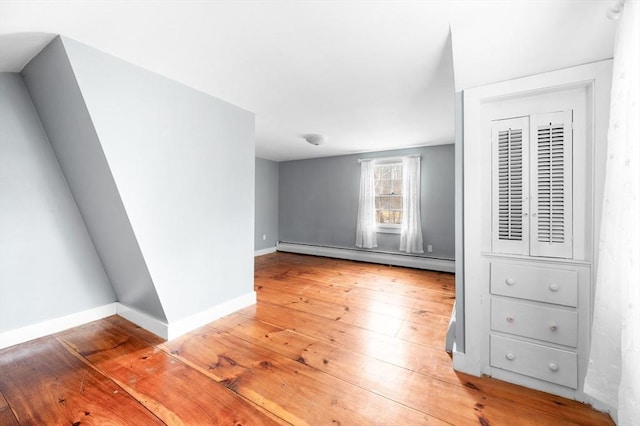 empty room featuring a baseboard heating unit, light wood-style flooring, and baseboards