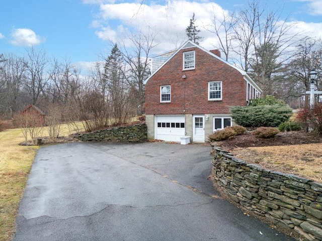 view of side of property with a garage, a chimney, aphalt driveway, and brick siding