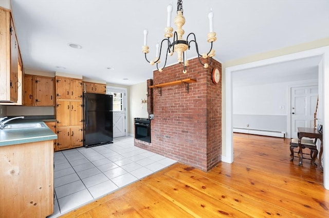 kitchen featuring light tile patterned floors, baseboard heating, freestanding refrigerator, a sink, and range