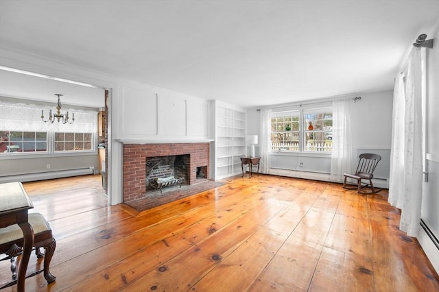 living room featuring a brick fireplace, a notable chandelier, wood-type flooring, and baseboard heating