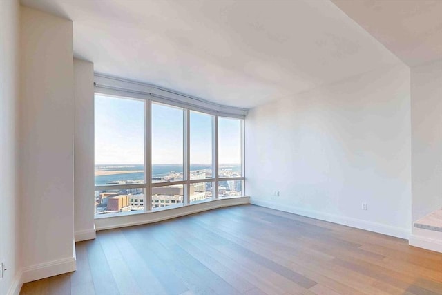 unfurnished room featuring baseboards, a wall of windows, a water view, and light wood-style floors