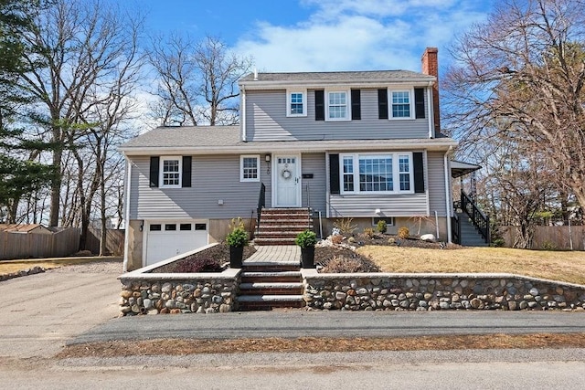 colonial home with an attached garage, fence, driveway, and a chimney