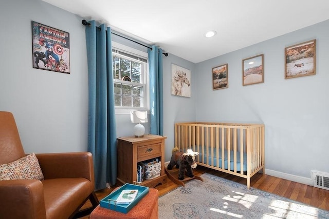 bedroom with visible vents, baseboards, a nursery area, and wood finished floors