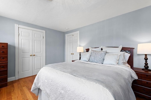 bedroom featuring baseboards, light wood-type flooring, a closet, and a textured ceiling