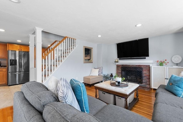 living room with stairway, light wood finished floors, decorative columns, recessed lighting, and a brick fireplace