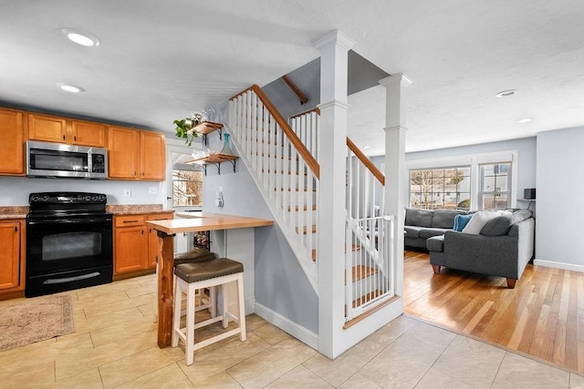 kitchen featuring baseboards, ornate columns, electric range, stainless steel microwave, and brown cabinets