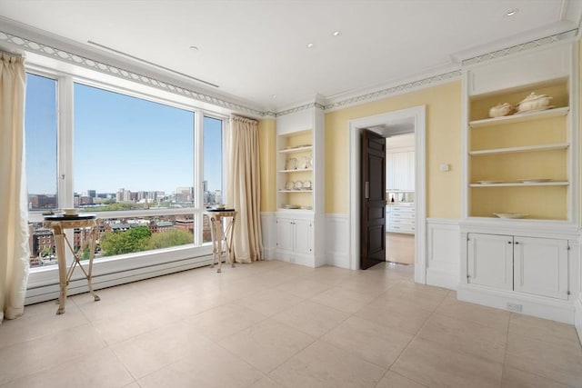 empty room featuring crown molding, built in features, a wainscoted wall, a view of city, and light tile patterned floors