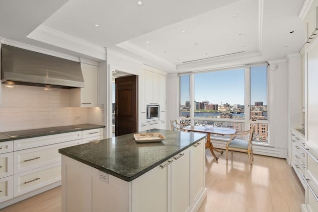 kitchen featuring wall chimney range hood, black electric stovetop, decorative backsplash, light wood-type flooring, and a tray ceiling