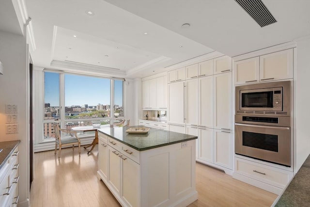 kitchen with appliances with stainless steel finishes, a raised ceiling, white cabinetry, light wood-type flooring, and visible vents