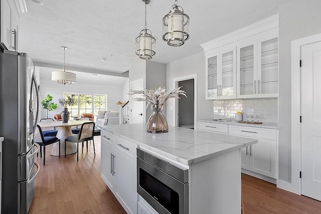 kitchen featuring stainless steel appliances, dark wood-type flooring, a center island, white cabinets, and light stone countertops