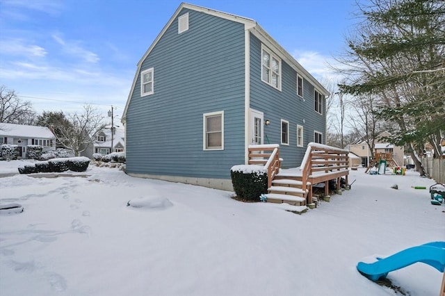 view of snowy exterior with a playground and a wooden deck