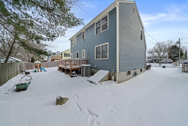 snow covered property with a wooden deck, central AC, and a playground