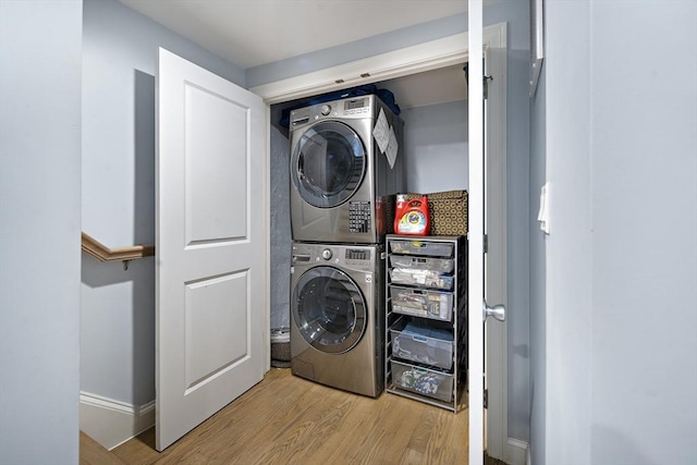 laundry area featuring stacked washer and clothes dryer, wood finished floors, and baseboards