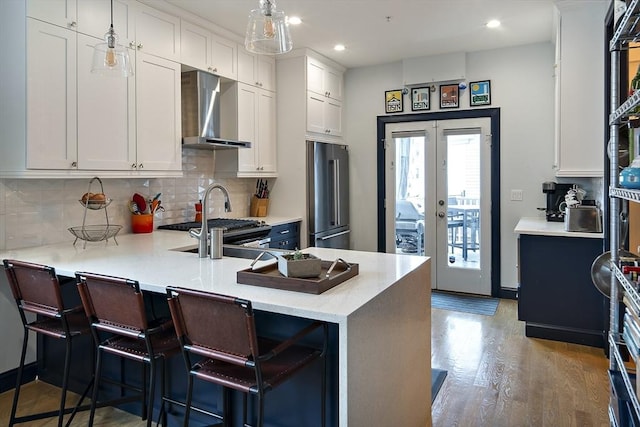 kitchen with wall chimney exhaust hood, high end fridge, french doors, light countertops, and decorative backsplash