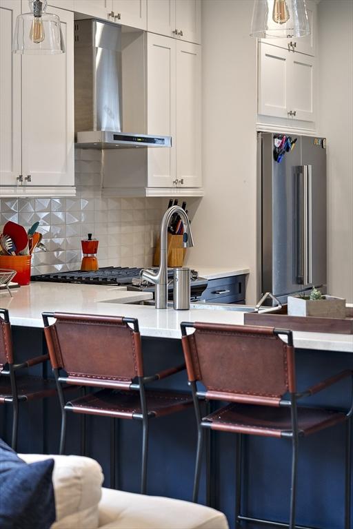 kitchen with wall chimney range hood, high end fridge, and white cabinets