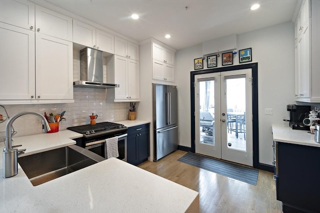 kitchen with stainless steel appliances, wall chimney exhaust hood, a sink, french doors, and light wood finished floors