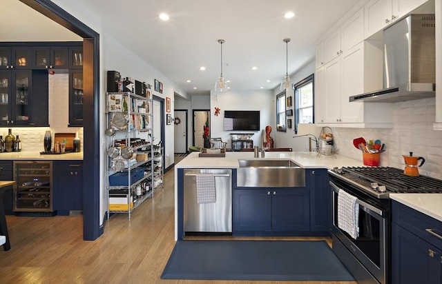 kitchen with stainless steel appliances, wall chimney range hood, a sink, wine cooler, and a peninsula