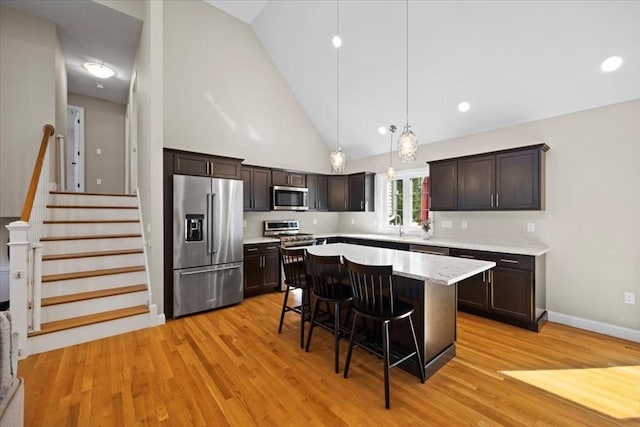 kitchen featuring stainless steel appliances, dark brown cabinets, a breakfast bar area, and light wood finished floors