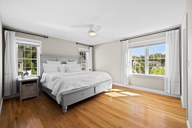 bedroom with a ceiling fan, multiple windows, wood finished floors, and baseboards