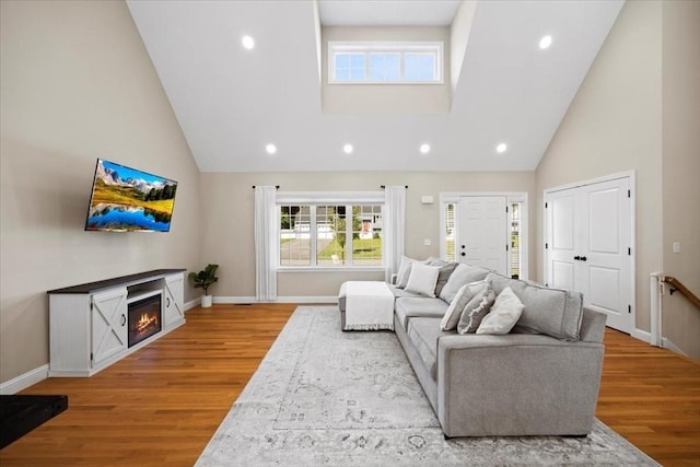 living area with baseboards, high vaulted ceiling, recessed lighting, a glass covered fireplace, and light wood-type flooring