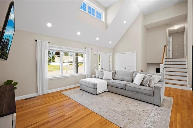 living room featuring light wood finished floors, stairway, high vaulted ceiling, and baseboards