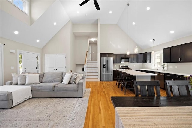 living area featuring stairway, light wood-style floors, and high vaulted ceiling