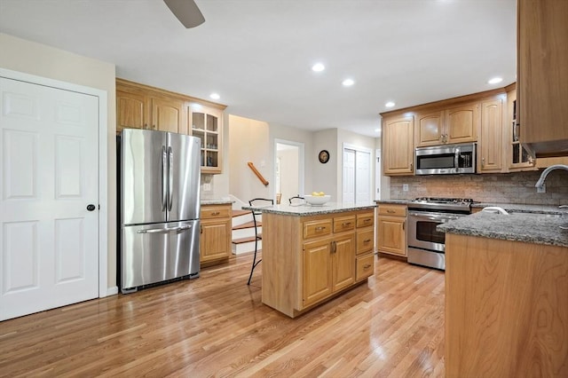 14 Nourse St, Westborough, MA 01581 - kitchen featuring appliances with stainless steel finishes, light wood-style flooring, dark stone counters, decorative backsplash, and a kitchen island