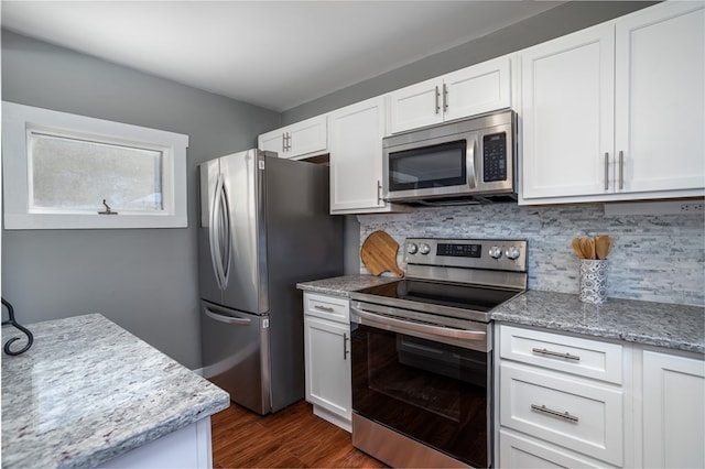 kitchen with appliances with stainless steel finishes, white cabinetry, dark wood-type flooring, light stone counters, and backsplash