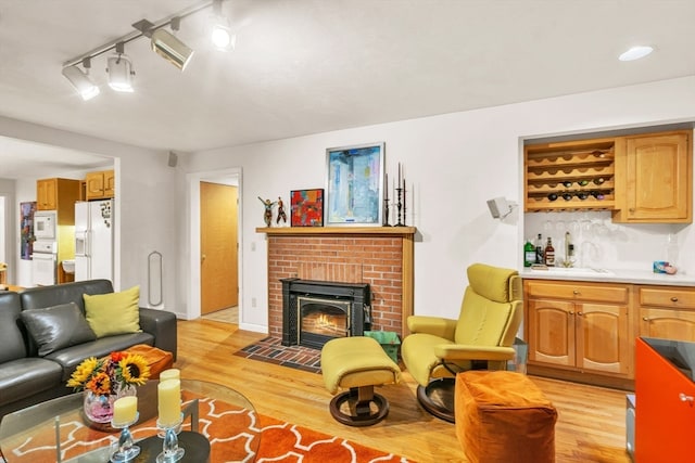 living room with light wood-type flooring, a fireplace, track lighting, and wet bar