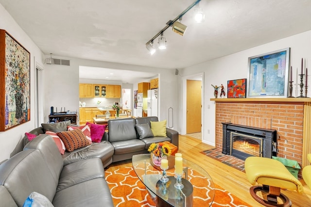 living room featuring track lighting, light hardwood / wood-style floors, and a brick fireplace