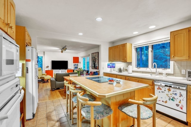 kitchen featuring a breakfast bar area, white appliances, tile countertops, light hardwood / wood-style floors, and sink