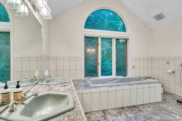 bathroom with tile walls, lofted ceiling, a relaxing tiled tub, and sink