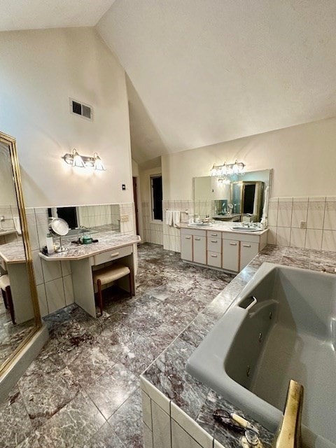 bathroom featuring a tub, vaulted ceiling, vanity, backsplash, and tile walls