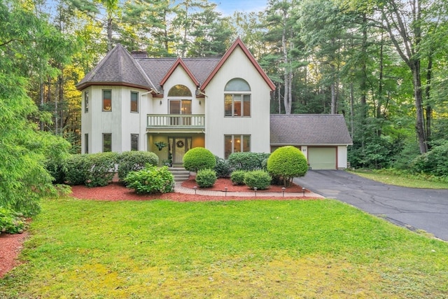 english style home featuring a balcony, a garage, and a front lawn