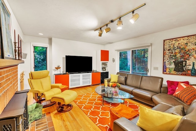 living room featuring wood-type flooring, a brick fireplace, and track lighting