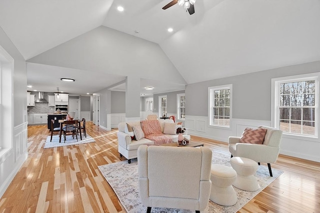 living room with ceiling fan, light wood-type flooring, and high vaulted ceiling