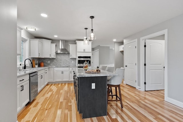 kitchen with white cabinetry, light hardwood / wood-style flooring, a kitchen island, and wall chimney range hood