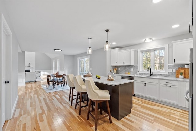 kitchen featuring a center island, white cabinets, sink, light hardwood / wood-style flooring, and light stone countertops