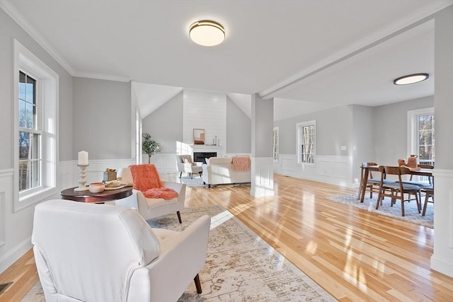 living room featuring vaulted ceiling, ornamental molding, a fireplace, and light hardwood / wood-style flooring