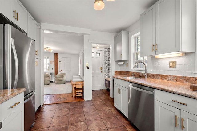 kitchen featuring tasteful backsplash, white cabinetry, sink, light stone counters, and stainless steel appliances